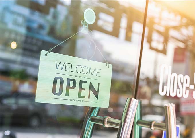 A sign in a storefront that reads "welcome, we're open"